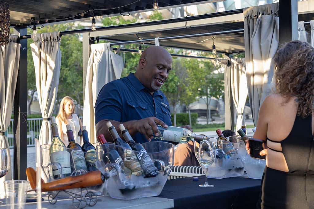 Guests enjoying wine tasting at an outdoor event with a bartender serving drinks at a restaurant patio