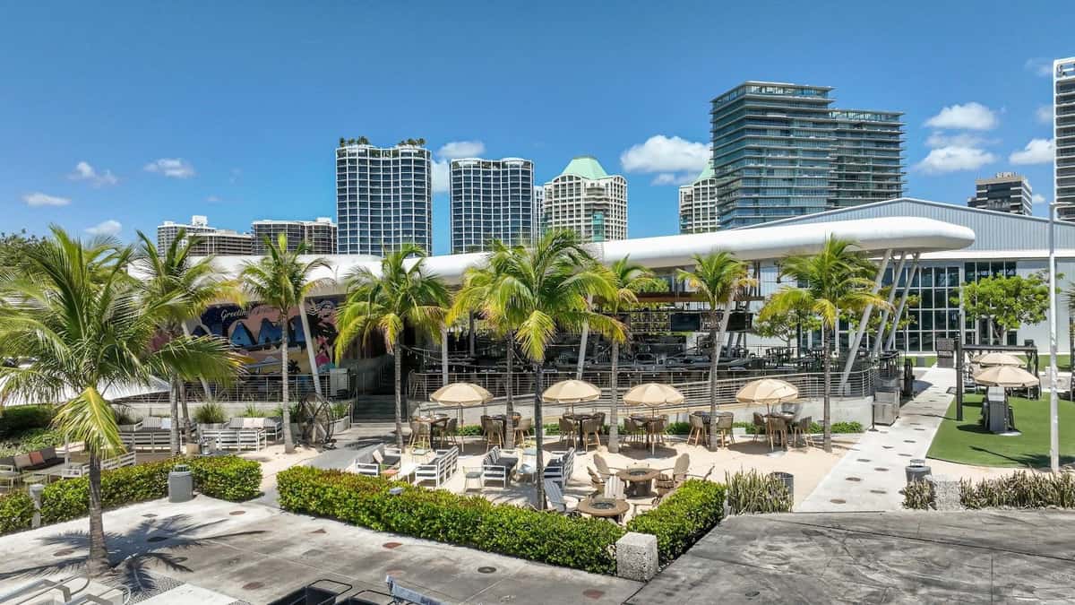 Bayshore Club waterfront patio with palm trees, outdoor seating, and Miami skyline views.