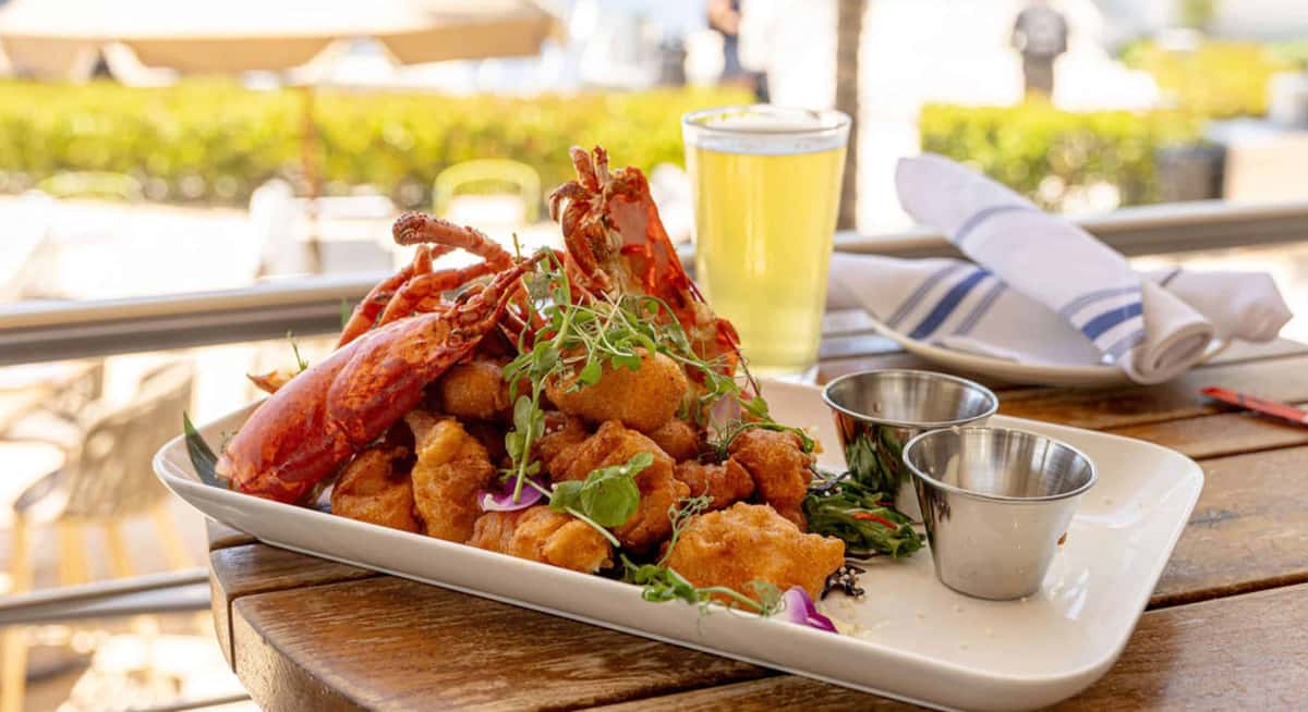 Seafood platter with lobster and fried bites served on a wooden table with beer at a waterfront restaurant.