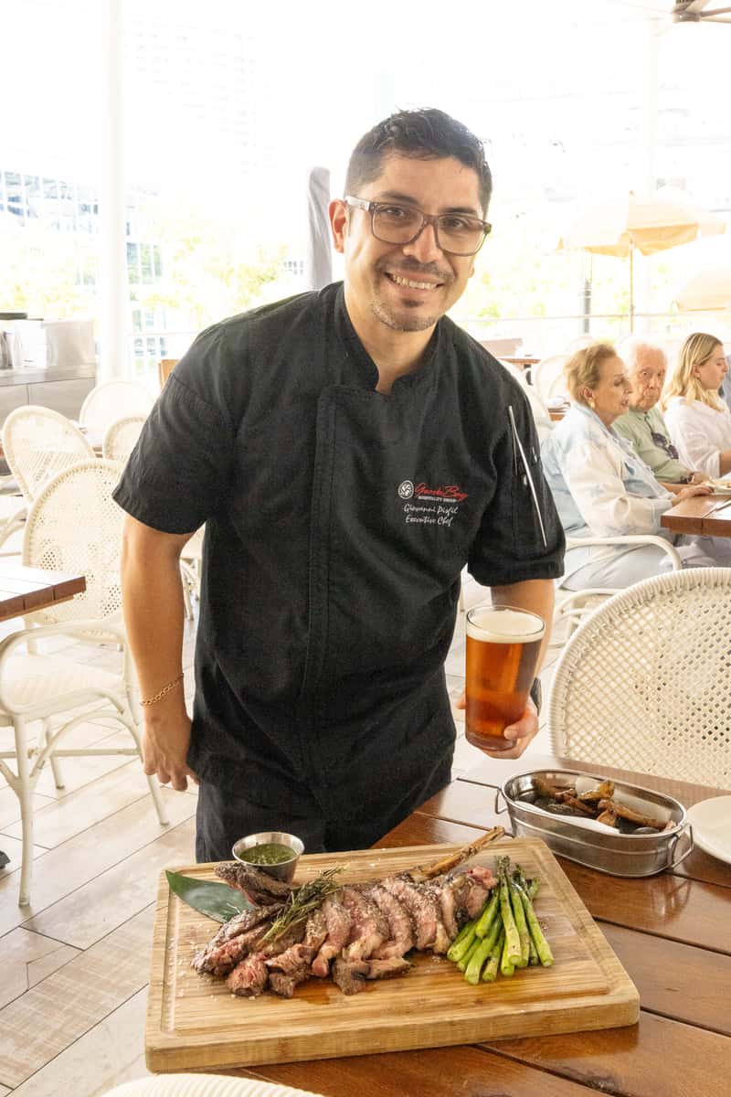 Executive chef presenting a sliced tomahawk steak with grilled asparagus and a glass of beer.