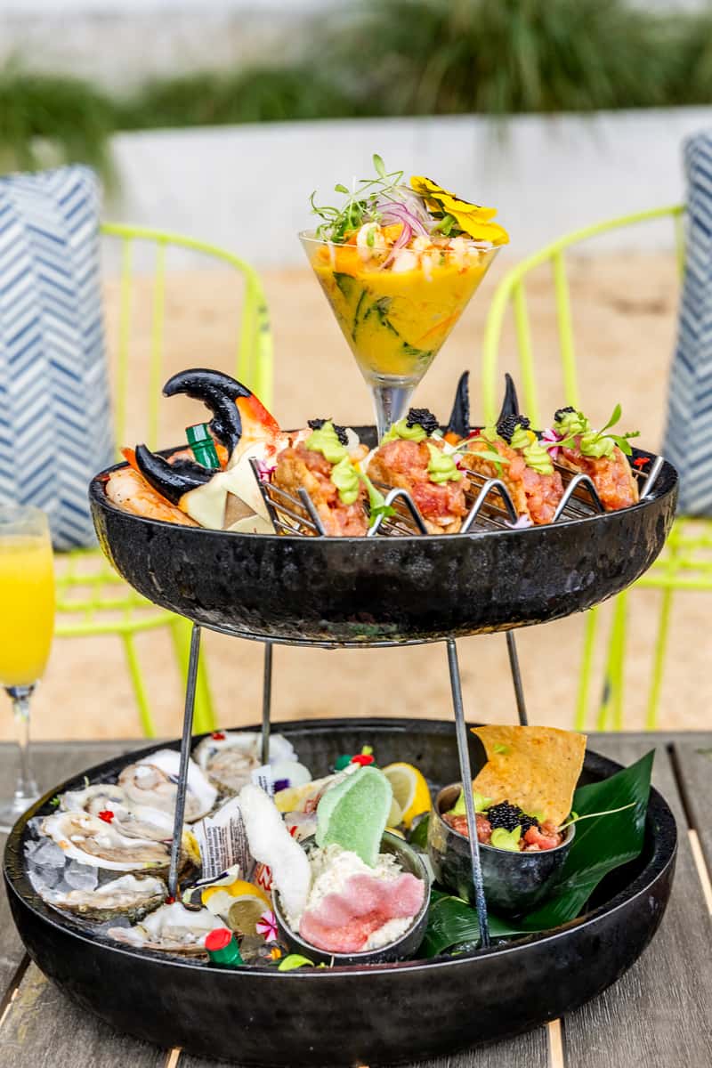 Gourmet seafood tower with oysters, tacos, ceviche, sauces, and tropical patio seating