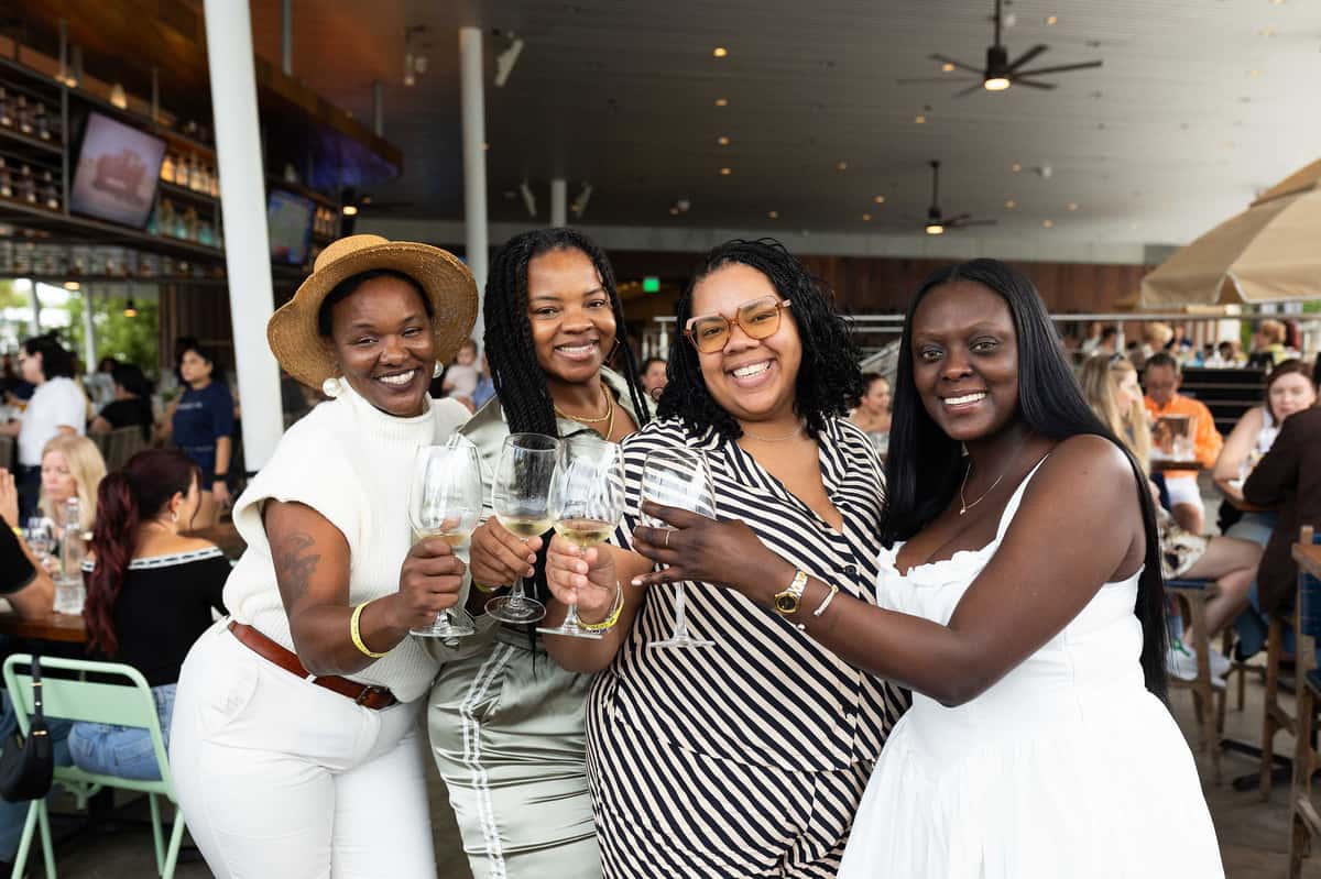 Four women smiling and holding wine glasses during a restaurant wine tasting event
