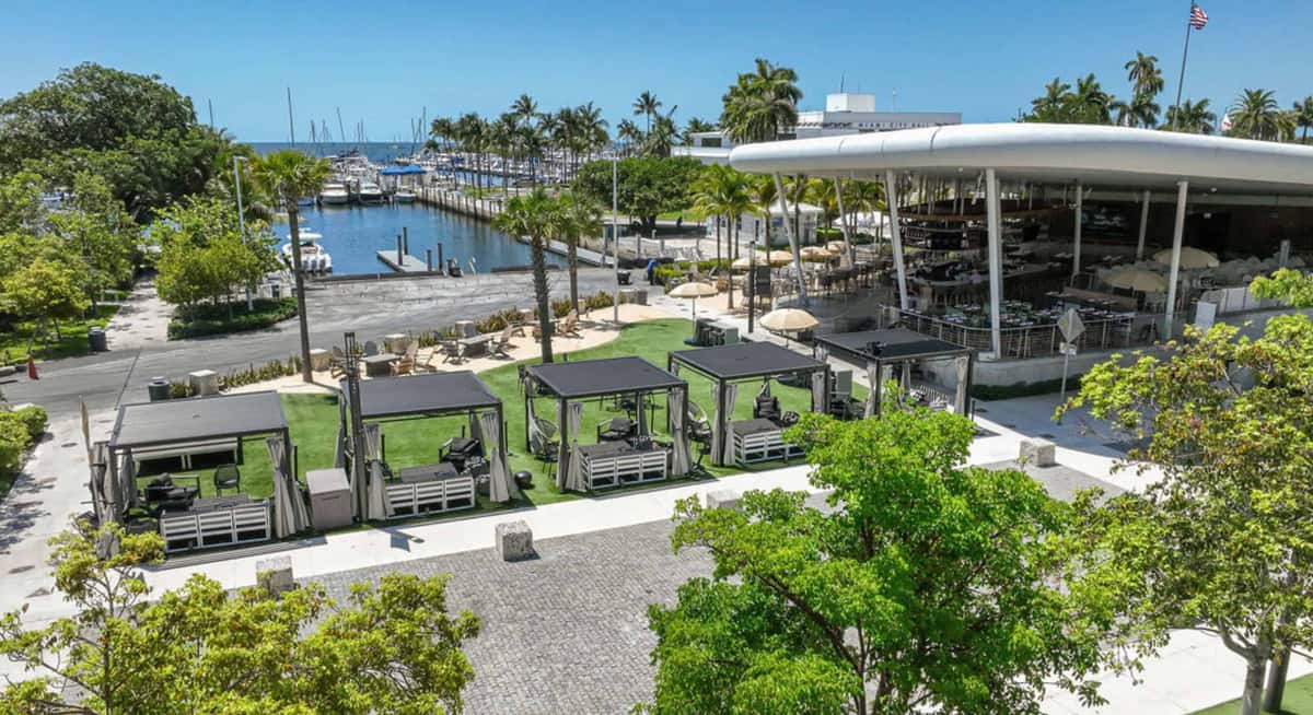 Aerial view of a waterfront restaurant with private cabanas, marina views, and palm-lined outdoor seating in Coconut Grove Miami.