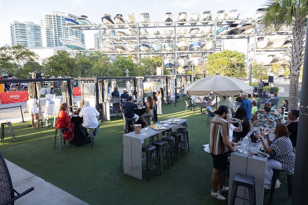 Outdoor restaurant event space with guests dining, lounge seating, umbrellas, and waterfront surroundings