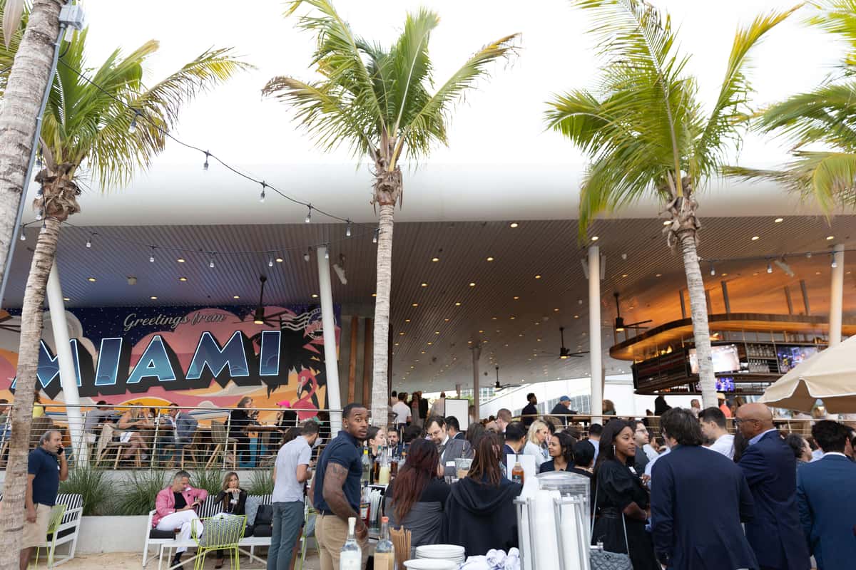 Lively outdoor social event at Bayshore Club with palm trees, a Miami mural, and guests gathered around the bar.