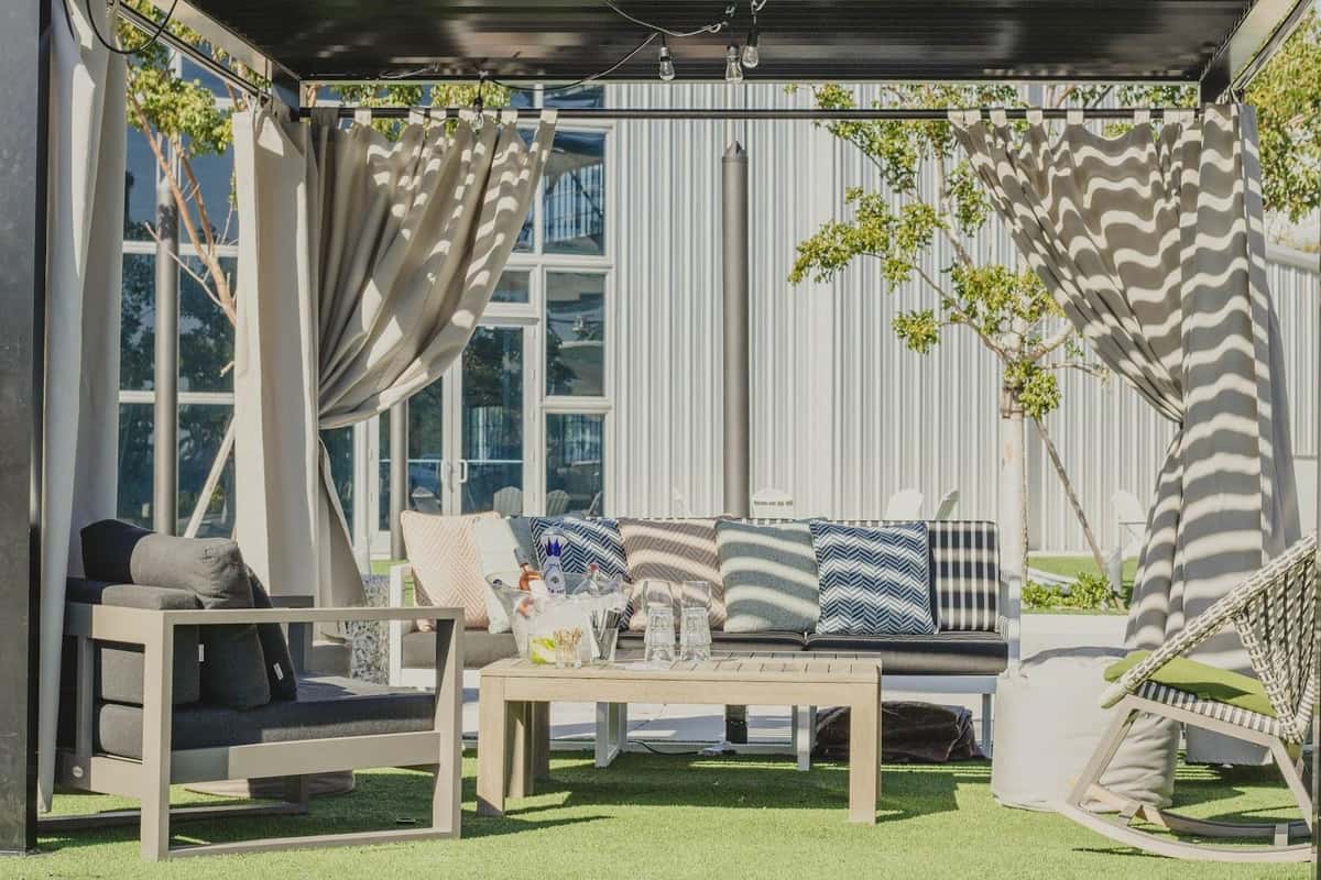 Shaded waterfront cabana seating with curtains, lounge chairs, and patterned pillows.