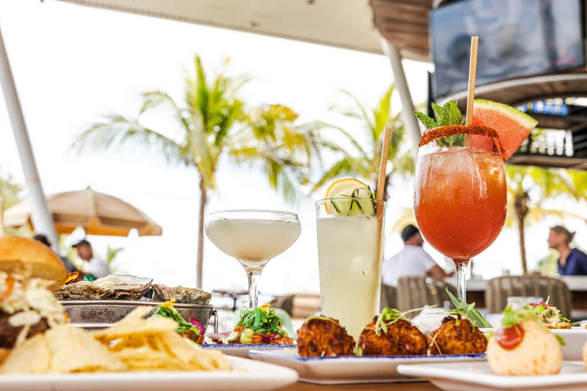 Tropical outdoor restaurant table with cocktails, oysters, and appetizers under palm trees