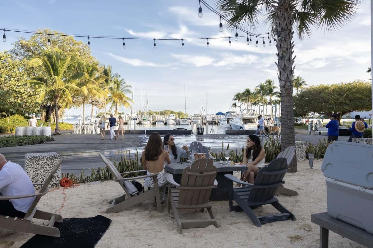Waterfront lounge seating at Bayshore Club overlooking the marina with string lights and palm trees.