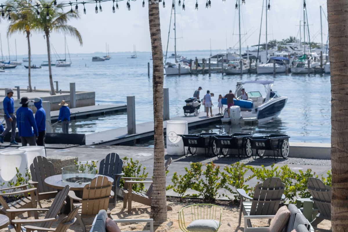 Outdoor waterfront seating overlooking Biscayne Bay with boats docked at a marina and people preparing to board a boat in Coconut Grove, Miami.