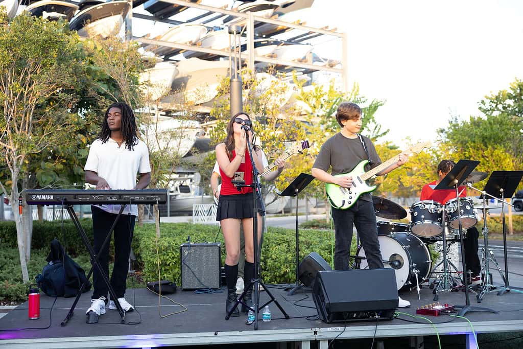 Live band performing outdoors with musicians playing keyboard, guitar, drums, and singing at an event