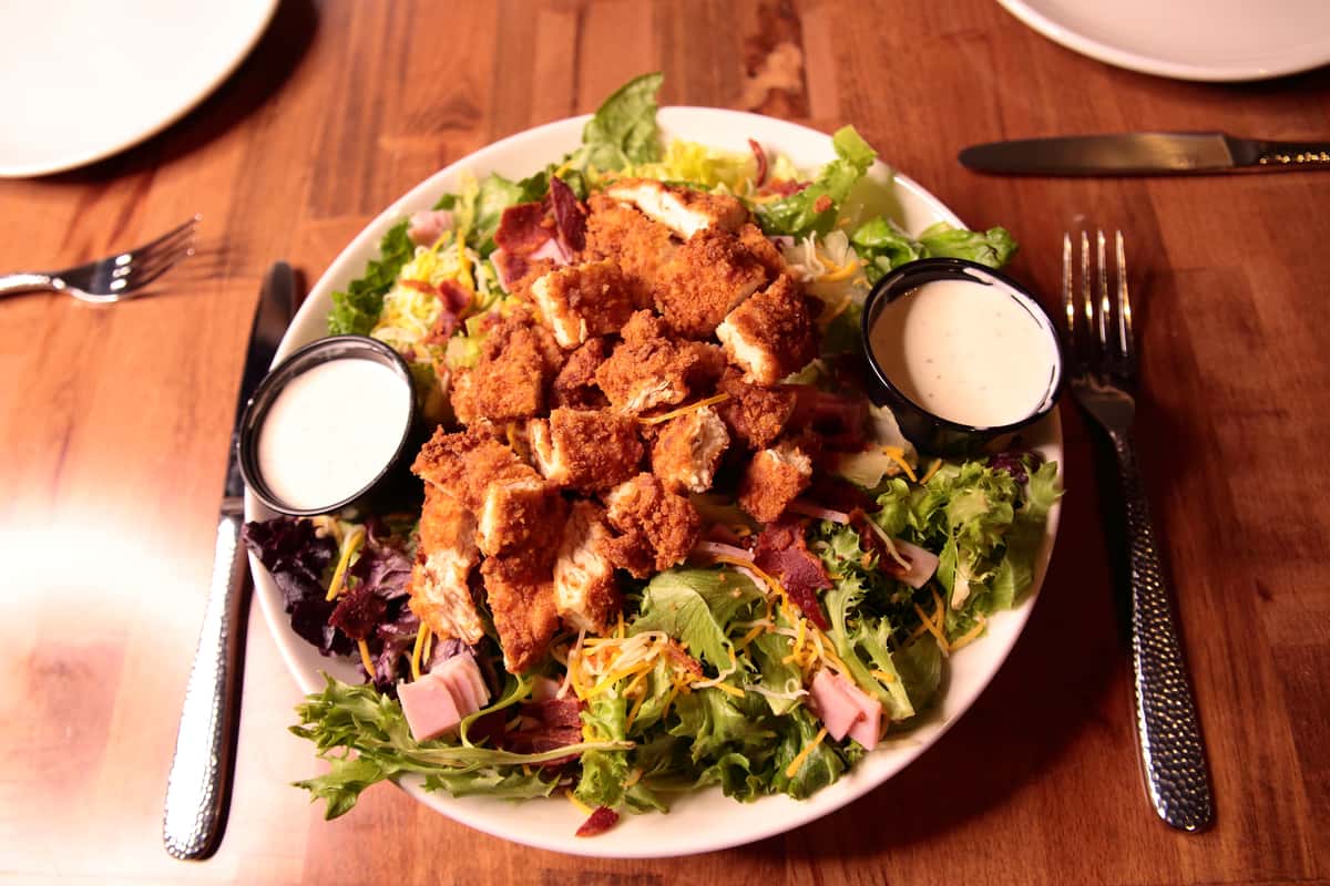 Crispy chicken tenders over romaine and mixed baby greens with sharp cheddar and Monterey jack cheeses, crumbled bacon, ham and grape tomatoes. Choice of dressing.