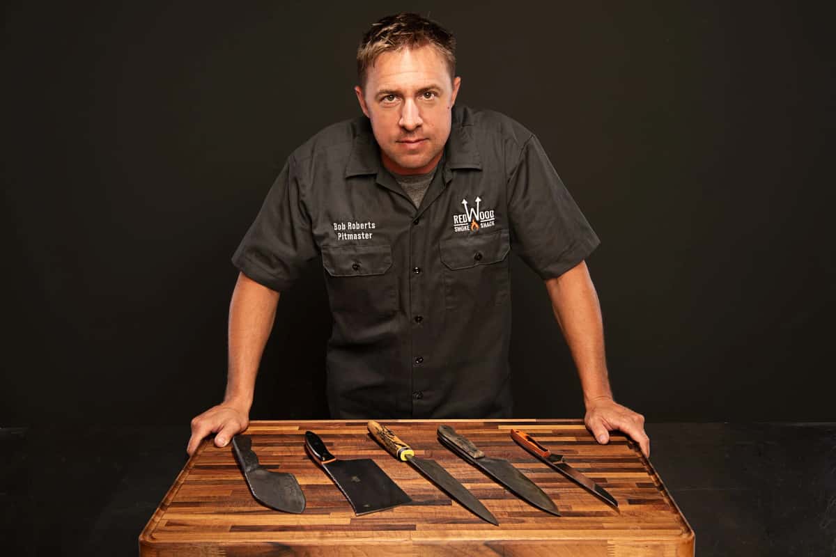 Bob Roberts posing in front of a cutting board with a variety of chef knives