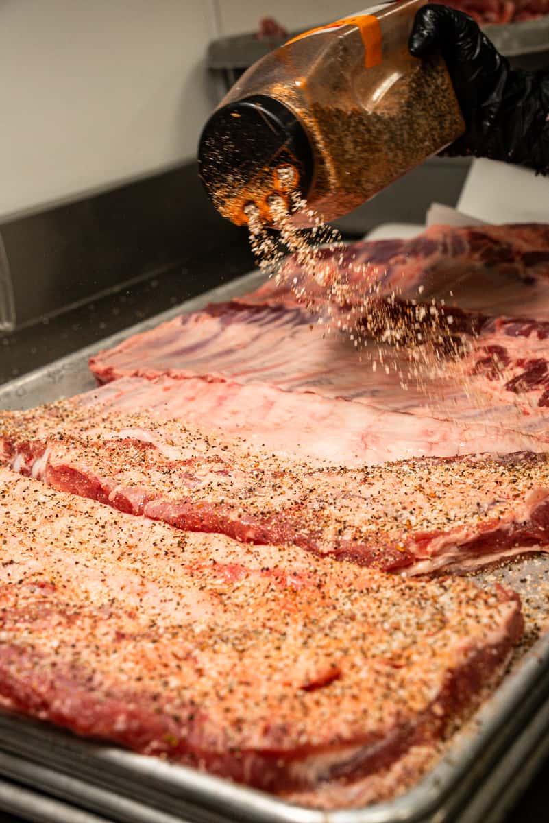 Hands seasoning large racks of ribs
