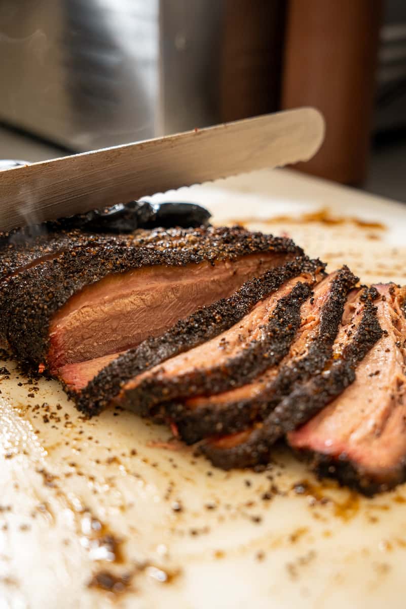Closeup of a knife slicing beef brisket on a cutting board