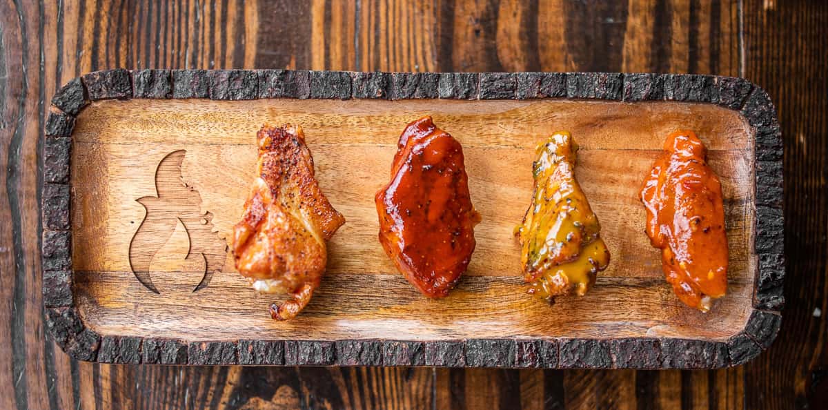 Four differently flavored wings lined up on a wood board