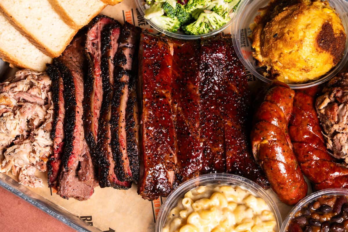 A bbq platter with sliced brisket, smoked sausage and ribs with sides of broccoli salad and macaroni and cheese