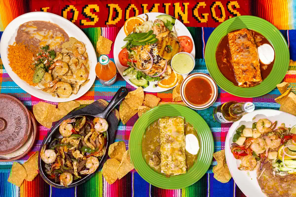 Multiple dishes prepared at Los Domingos atop a colorful table cloth embroidered with Los Domingos