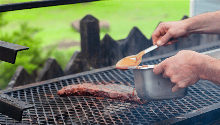 person putting sauce on ribs on the grill