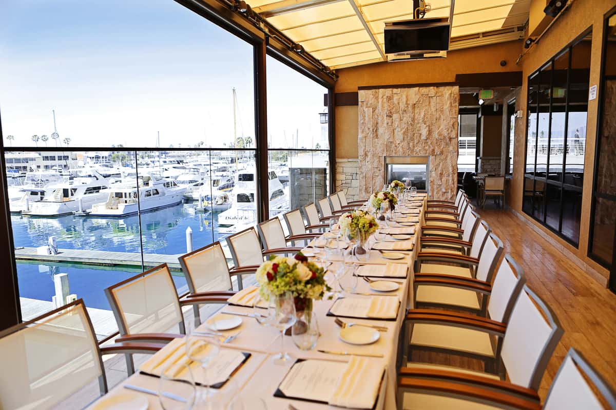 long dining table, set with menus, napkins, silverware, plates, flowers, over looking the marina