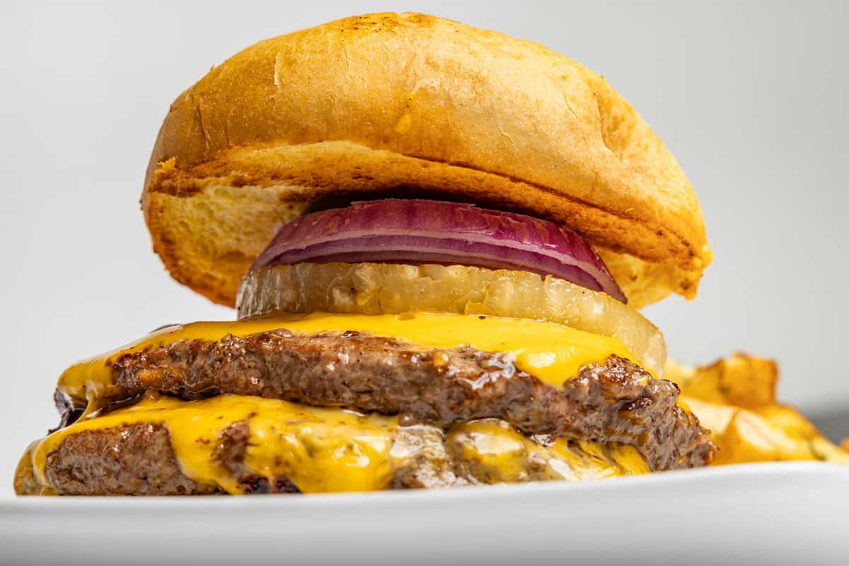 Get ready to level up your lunch. Our double beef patty smash burger is stacked with gooey, melted American cheddar, tender grilled white onions, and a crisp ring of red onion for that perfect bite. All tucked into a buttery, toasted brioche bun and served with a side of golden fries. Come hungry, leave happy—only at Phillys. 🍔🔥