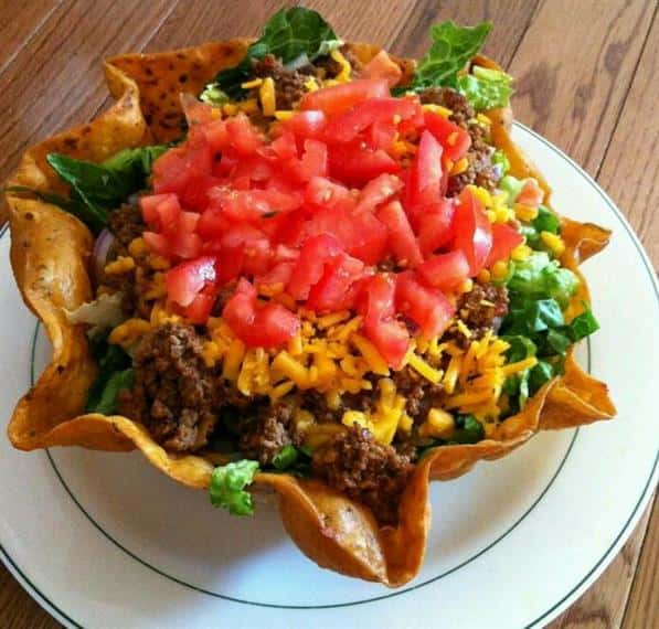 taco bowl salad with tomatoes and cheese on top of beef and lettuce