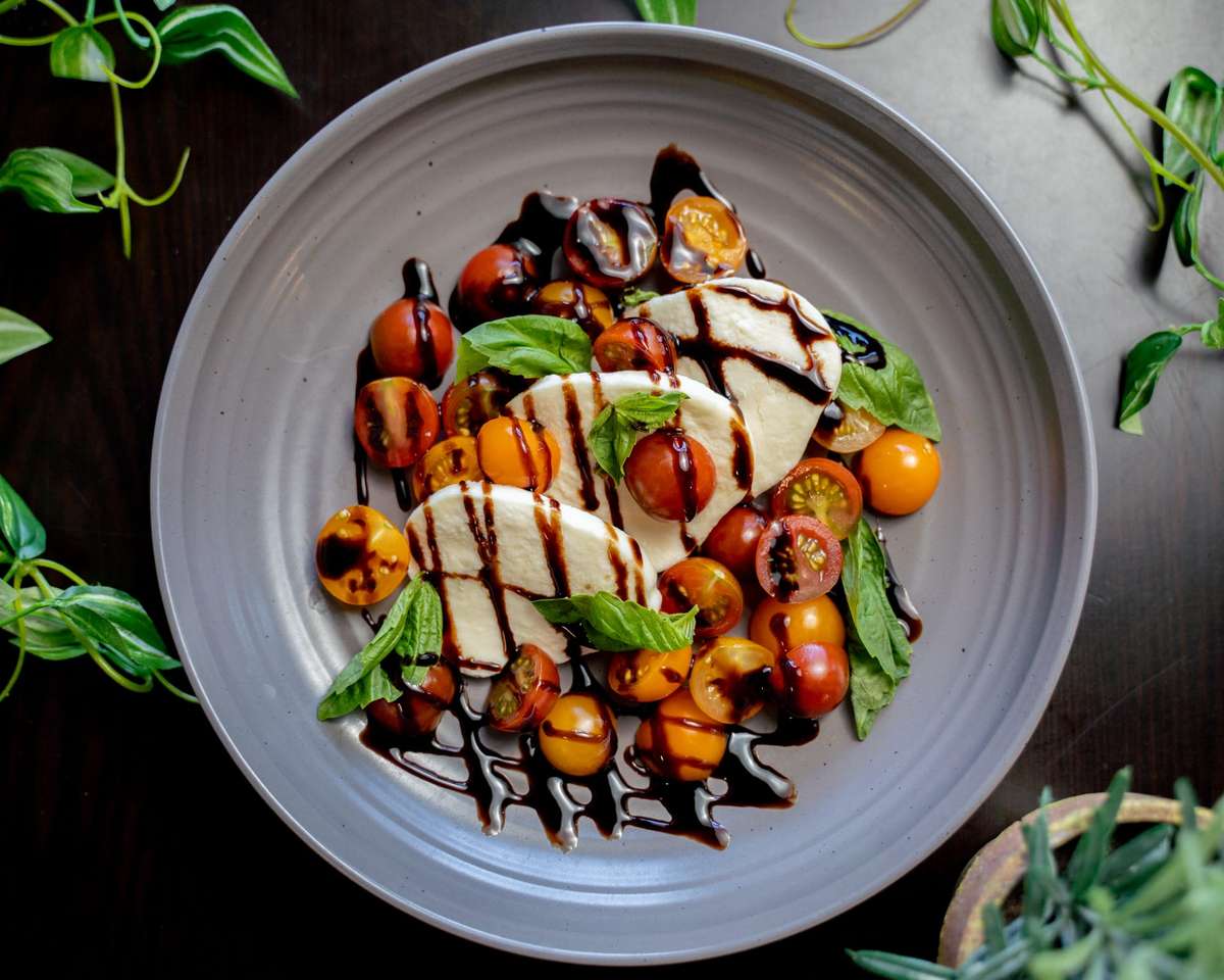 Vibrant Caprese salad with fresh mozzarella, colorful cherry tomatoes, basil, and balsamic glaze on a gray plate.