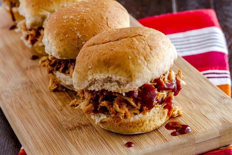 three barbeque sandwiches with barbeque sauce on a wooden board
