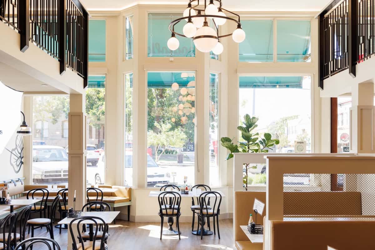 Bright dining room with tall windows, a chandelier, and bistro tables and chairs