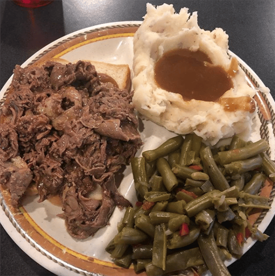 pulled pork sandwich with a side of string beans and mashed potatoes with gravy 