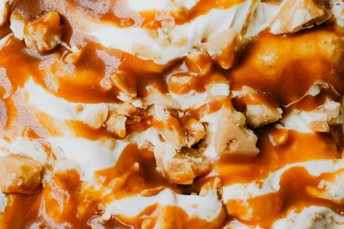 Close-up of vanilla ice cream swirled with caramel sauce and chunks of toffee or nuts.