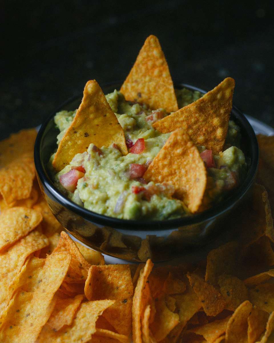 Nachos with guacamole and tomato in black bowl