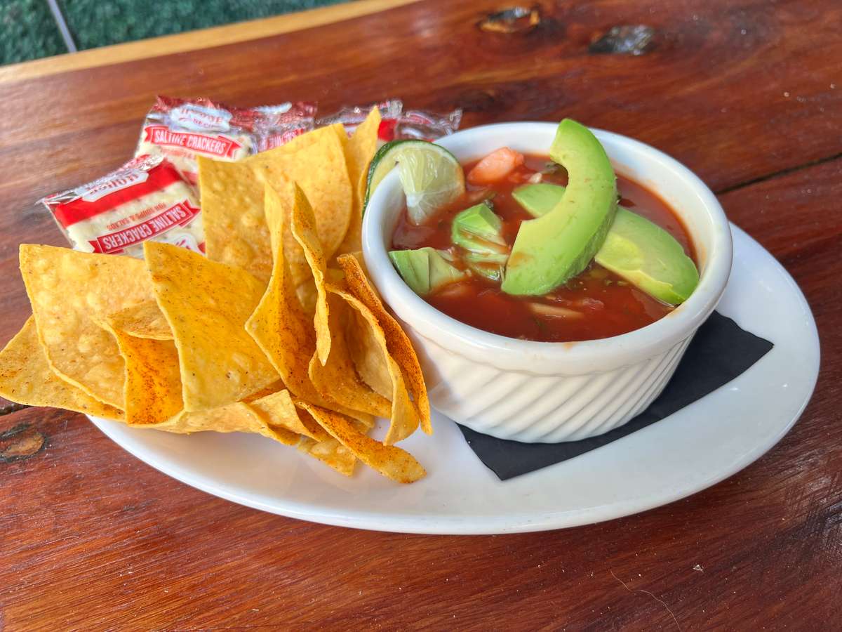 Tortilla chips served with avocado-topped tomato soup in a white bowl