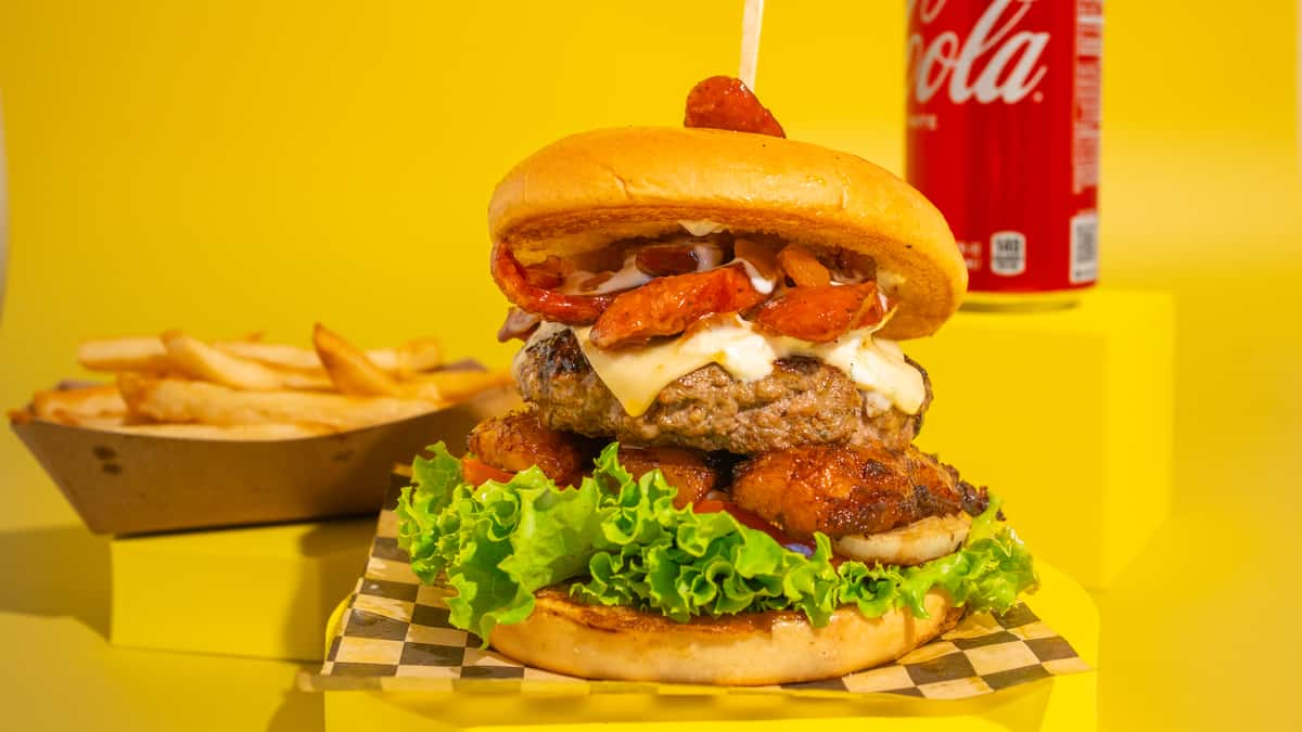 The Eternal Spring. Brioche bun, 100% handmade beef patty, caramelized chorizo, sweet plantain, cheese, lettuce, tomato, and grilled onions. House sauce and pineapple sauce. ALL OUR BURGERS AND HOT DOG ARE SERVED WITH FRIES! La Eterna Primavera - Pan brioche, carne de res 100% artesanal, chorizo caramelizado, plátano maduro, queso, lechuga, tomate y cebolla a la parrilla. Salsa de la casa y salsa de piña. TODAS NUESTRAS BURGERS Y PERROS VIENEN CON PAPAS A LA FRANCESA INCLUIDAS