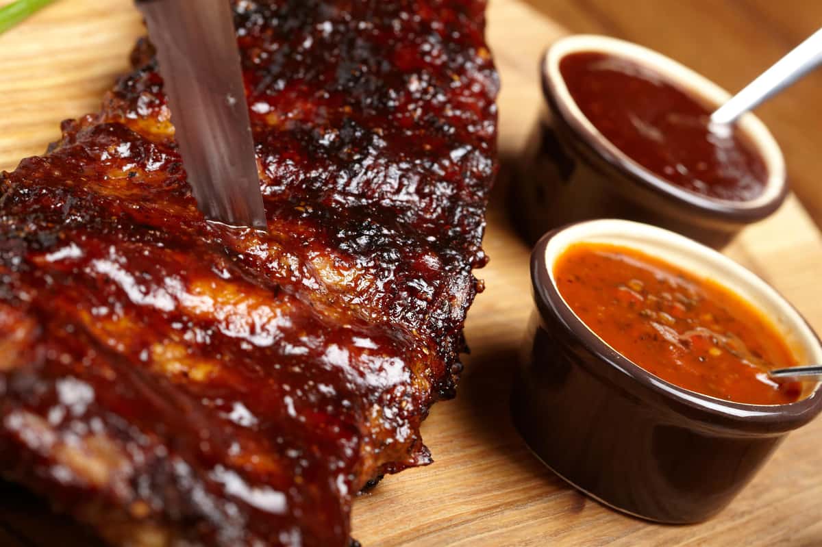 BBQ ribs on a wood table-top with small containers of sauce on the side