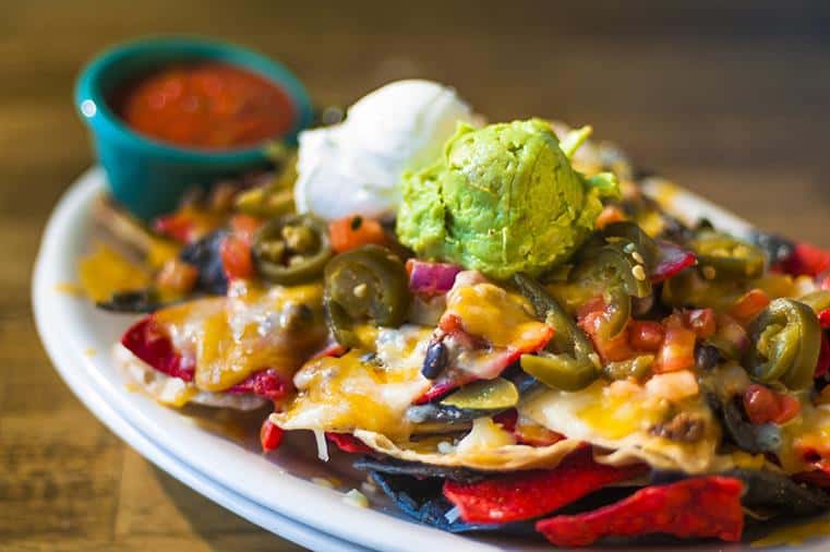Nachos with cheese, jalapenos, sour cream, guacamole, salsa on a dish.
