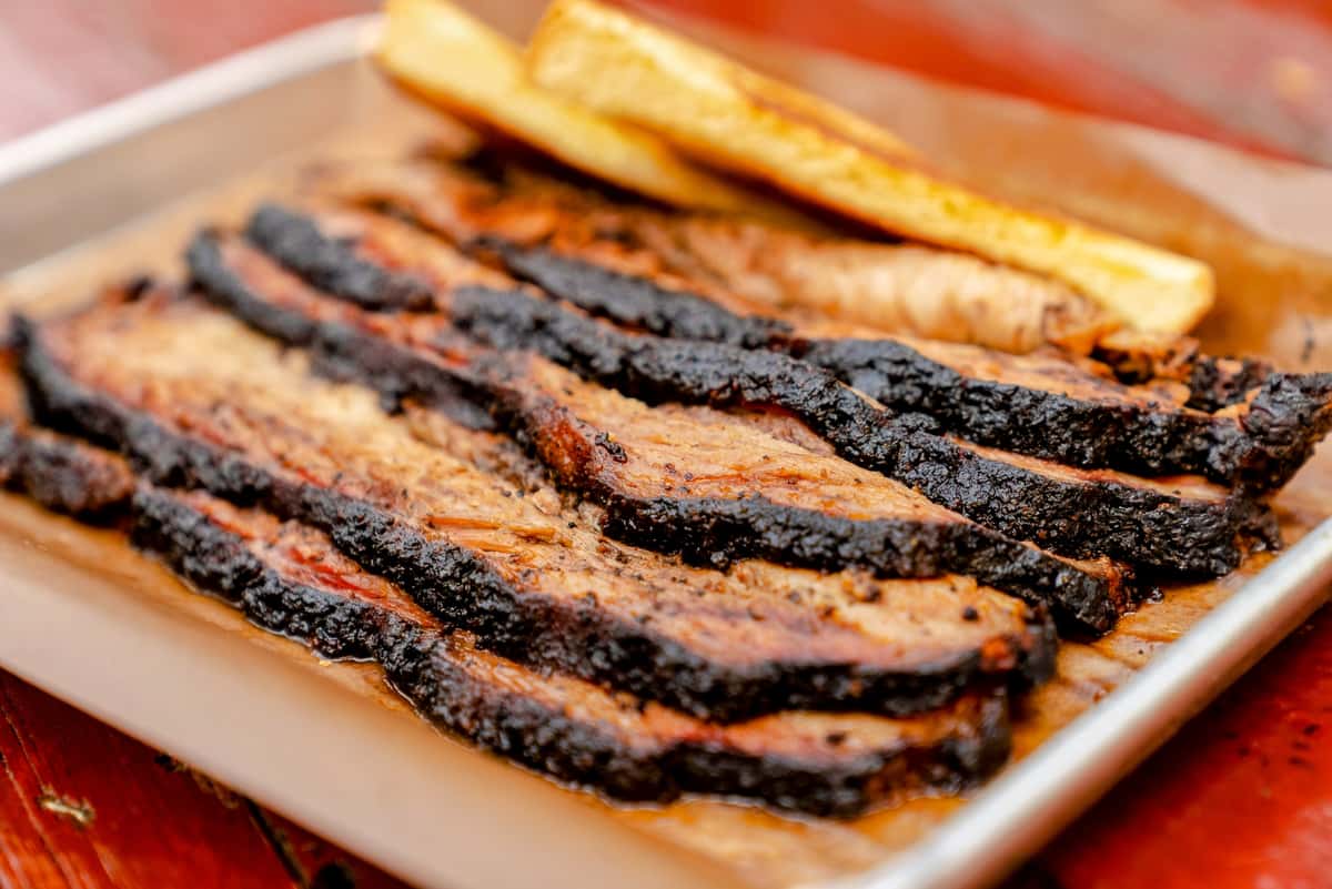 Sliced brisket with a dark bark, served with two pieces of toast.