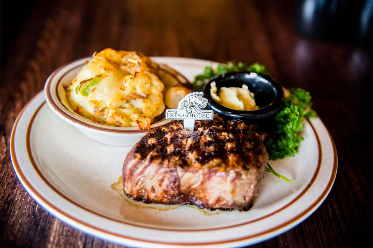 A perfectly grilled steak topped with sauce, paired with creamy mashed potatoes and fresh greens.