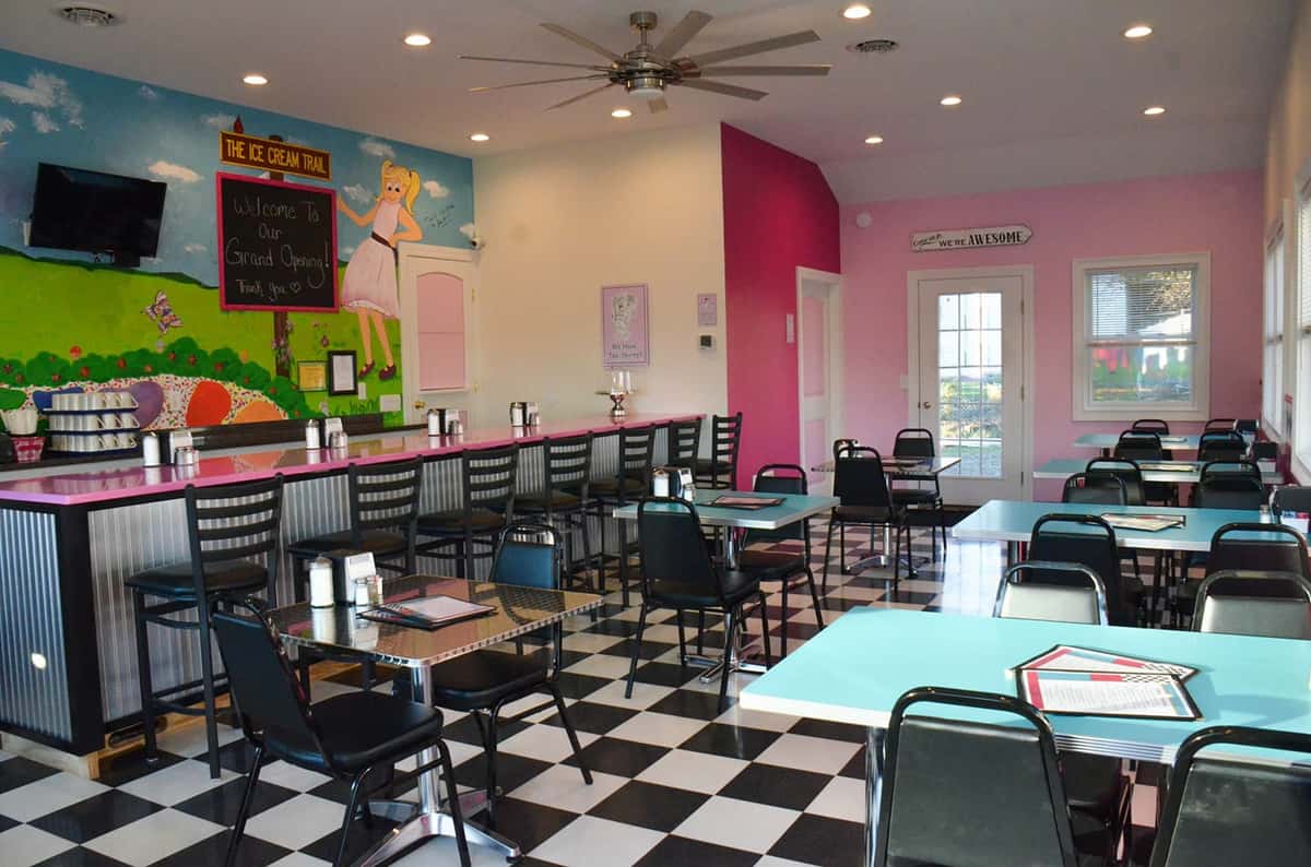 Bright and colorful retro-style ice cream parlor with pink walls, checkered floor, and teal dining tables.