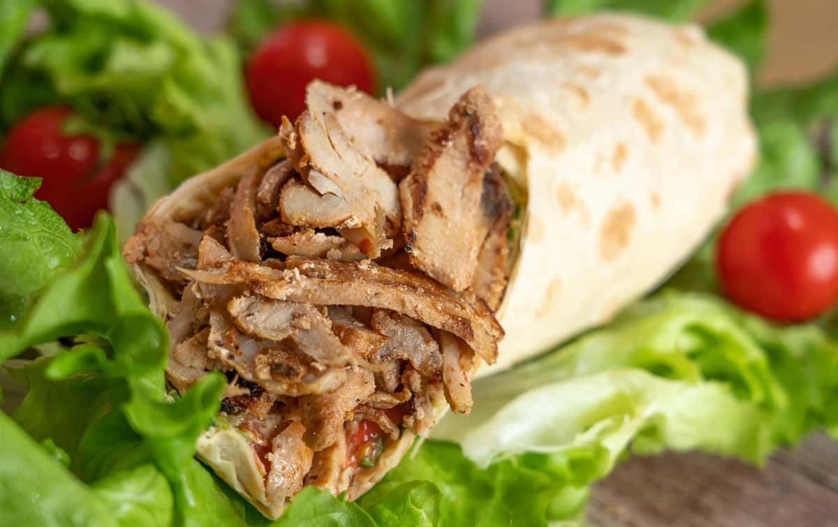 A close-up image of a grilled chicken wrap filled with tender slices of chicken, wrapped in a soft tortilla, and surrounded by fresh lettuce and ripe cherry tomatoes.