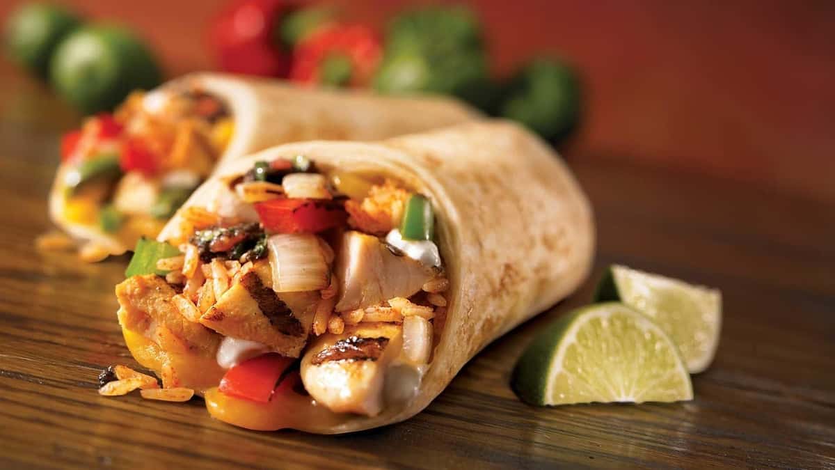 Grilled chicken burritos filled with rice, onions, peppers, and melted cheese, served with lime wedges on a wooden table.