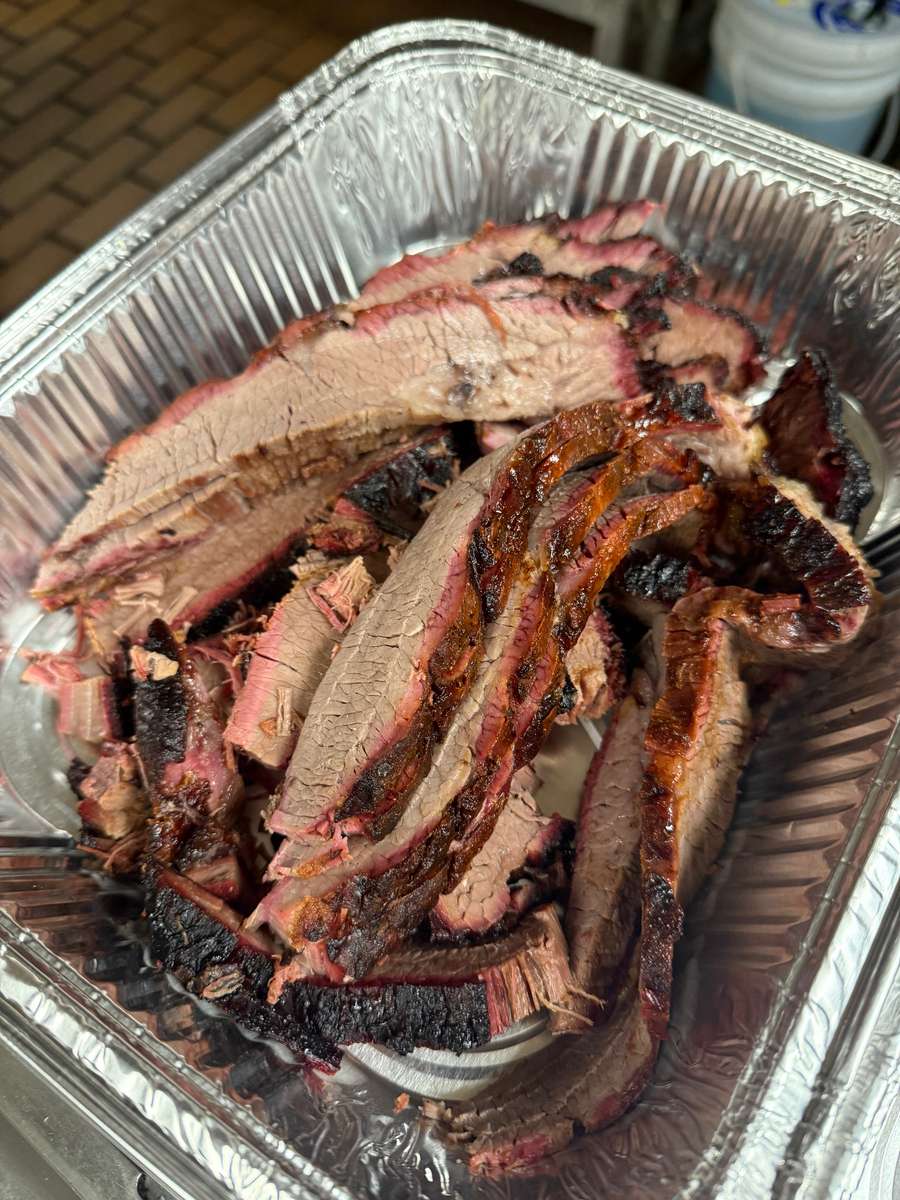 Tender, slow-smoked beef brisket sliced and served in a foil catering pan, showcasing a rich smoke ring and charred bark — perfect for BBQ lovers.