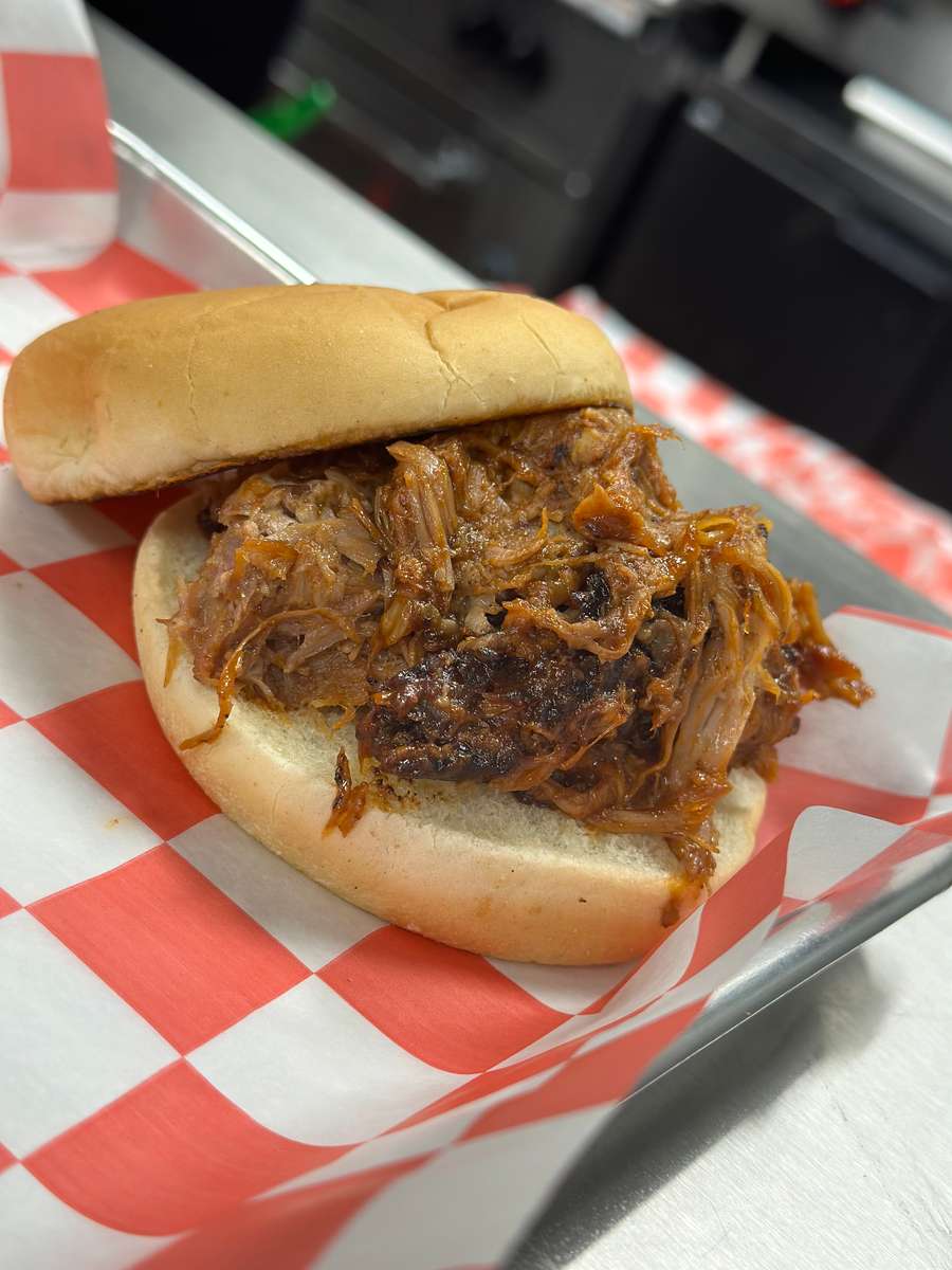 Classic BBQ pulled pork sandwich with tender, smoky shredded pork on a soft bun, served on a red and white checkered liner in a casual barbecue setting.