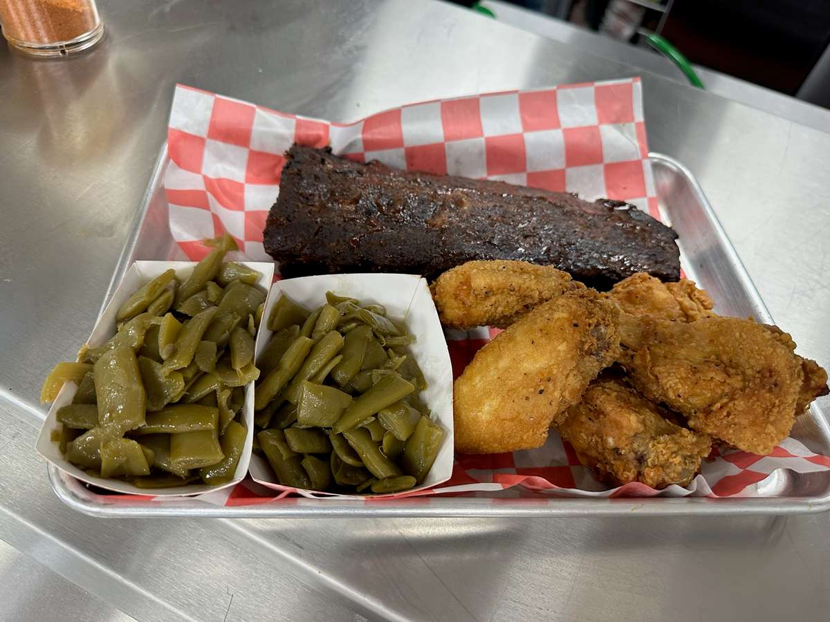 Southern BBQ combo plate featuring smoky pork ribs, crispy fried chicken, and two servings of tender green beans, served on a red checkered tray.