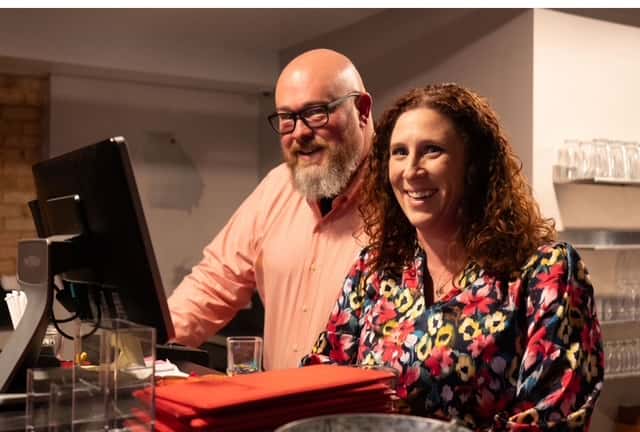 Two smiling restaurant owners stand together behind a counter