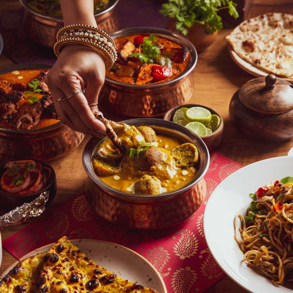 Indian curries with lady dipping roti in pot