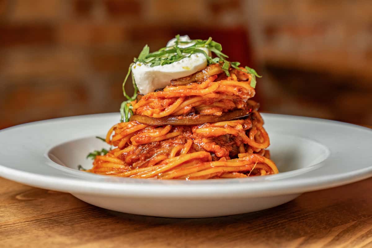 Stacked spaghetti alla Norma topped with fried eggplant, rich tomato sauce, creamy ricotta, and fresh basil, elegantly plated for a modern twist on a traditional Sicilian pasta dish.