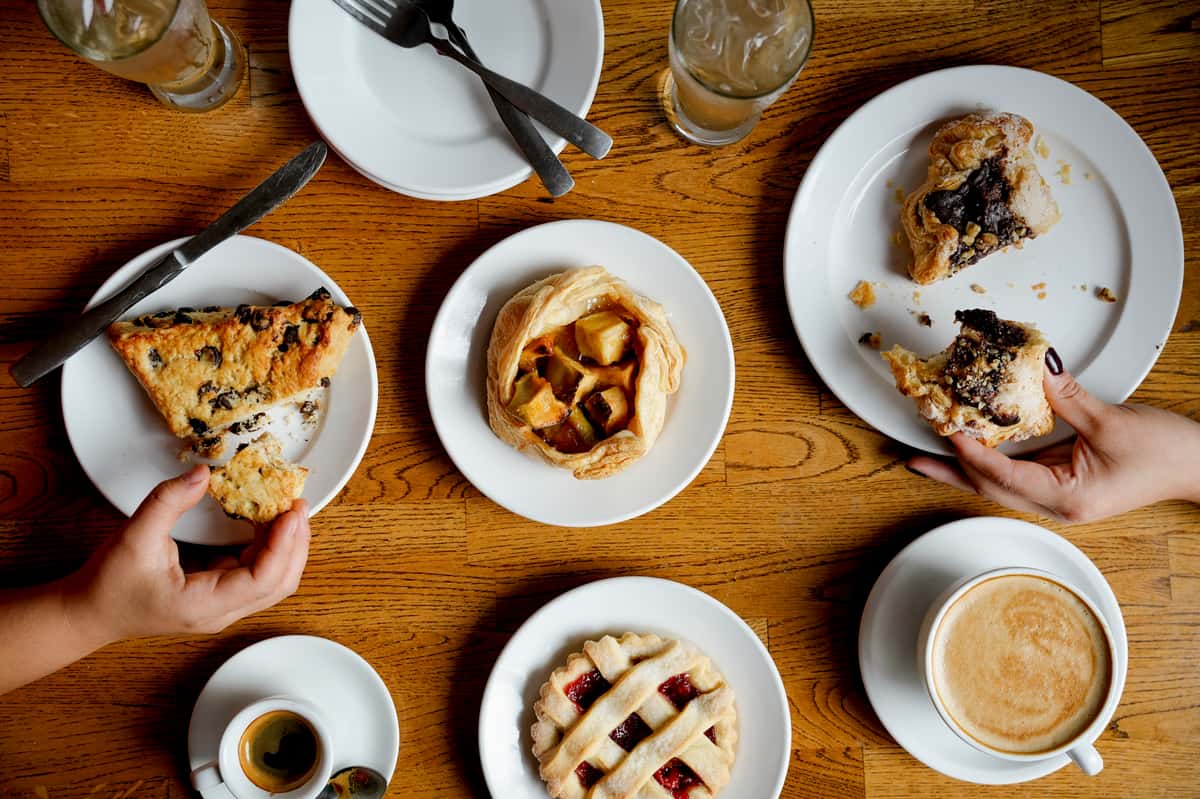 Cozy café brunch setting featuring a variety of artisan pastries, including a chocolate chip scone, fruit-filled lattice pie, apple galette, and chocolate-stuffed puff pastry, paired with espresso, iced beverages, and a creamy latte on a wooden table.