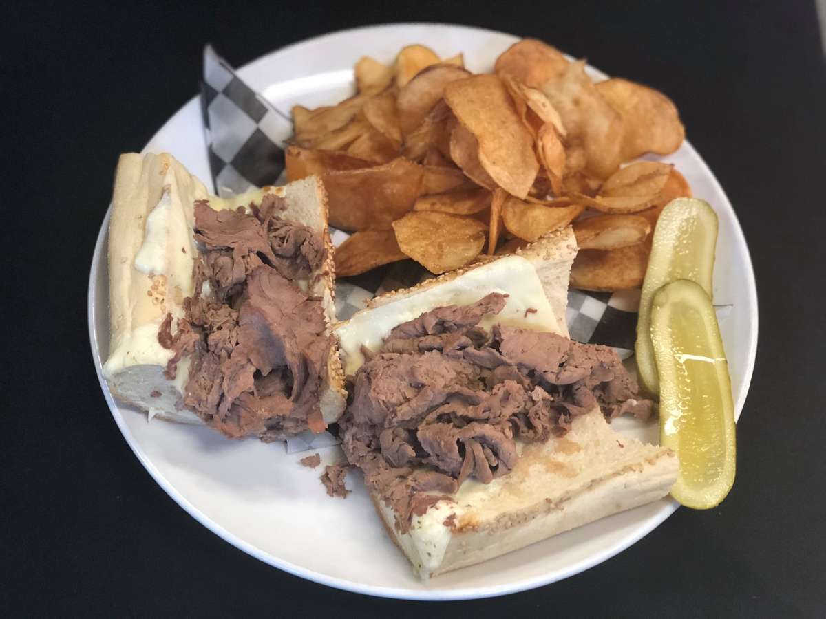 Open-face roast beef sandwich with pickles and potato chips
