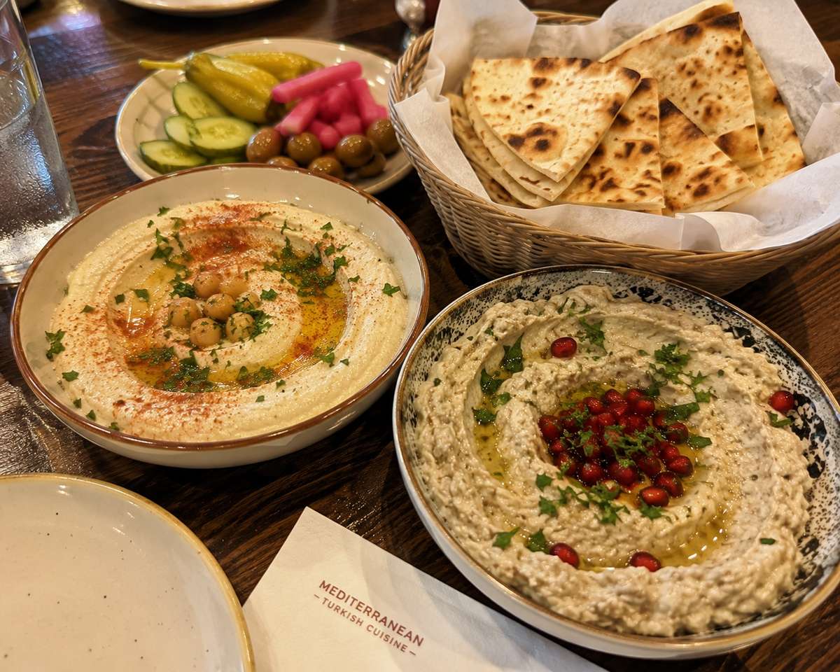 Creamy hummus and smoky babaganoush mezze served with warm pita bread, olives, and Mediterranean pickles