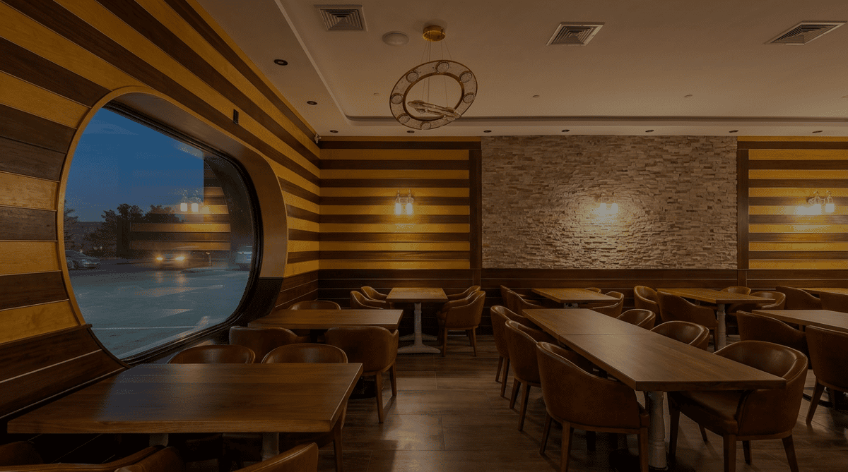 Restaurant interior with dark wood tables, brown leather chairs, striped and stone walls, and warm lighting.